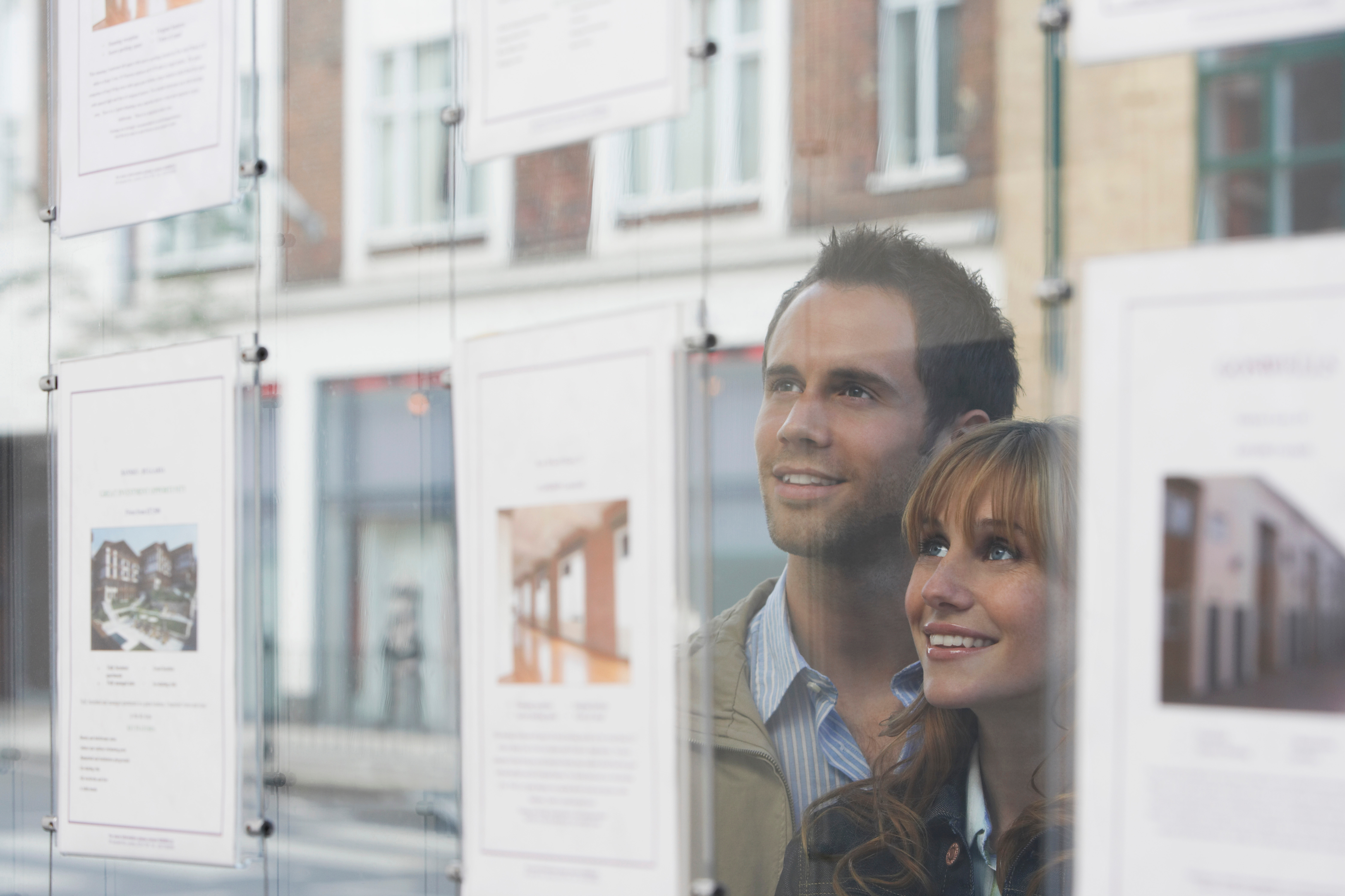 Jeune couple regardant la vitrine d'une agence immobilière 