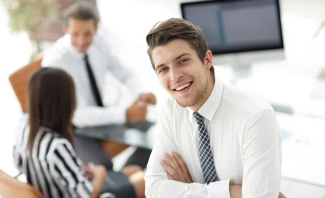Homme souriant devant une table avec une femme et un homme assis à un bureau